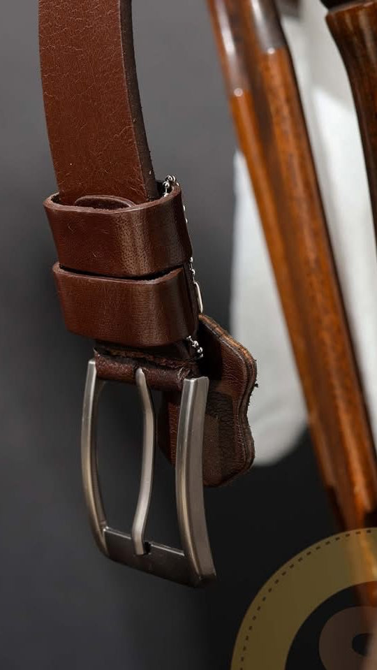 Brown leather belt with silver buckle on a dark background
