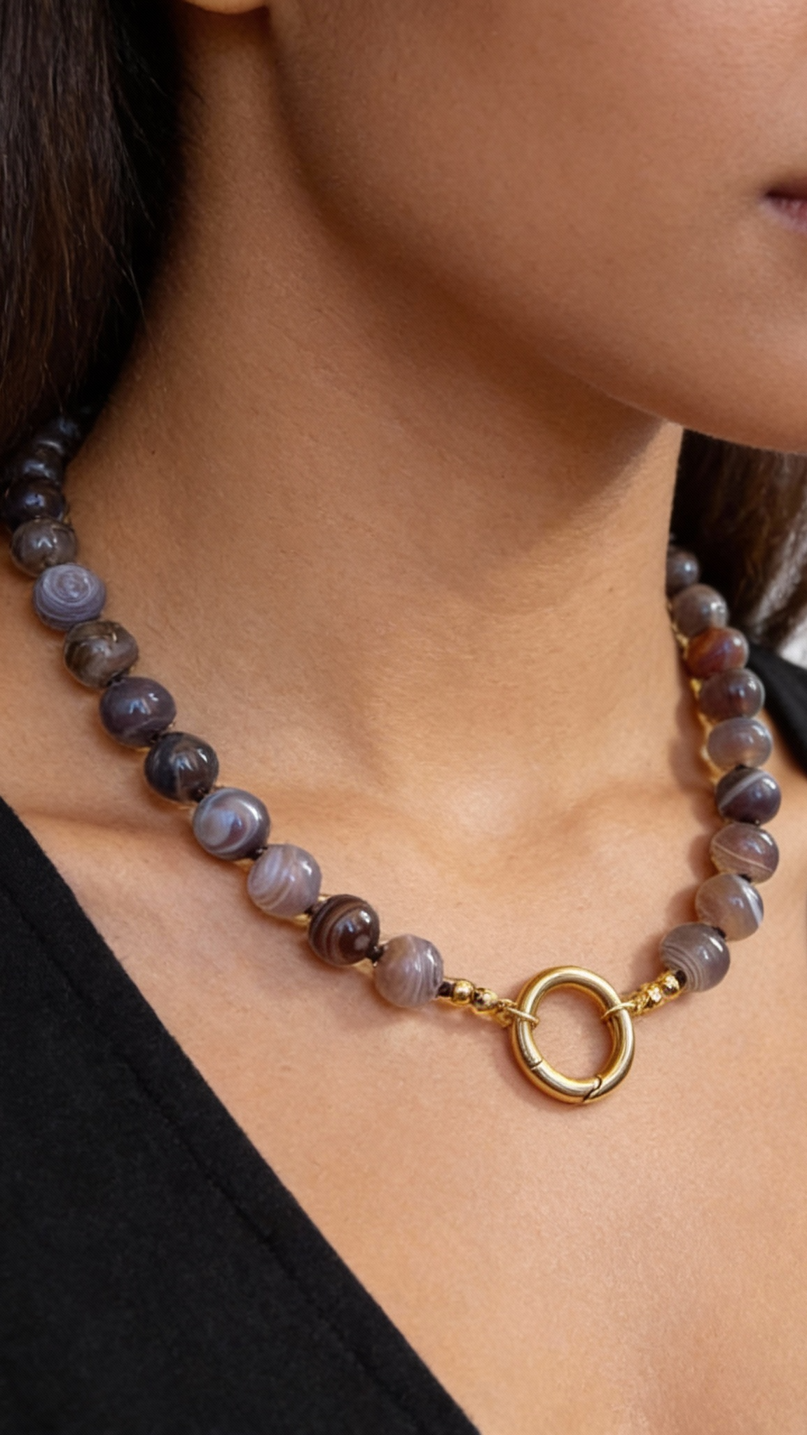 Necklace with a gold clasp worn by a person against a neutral background