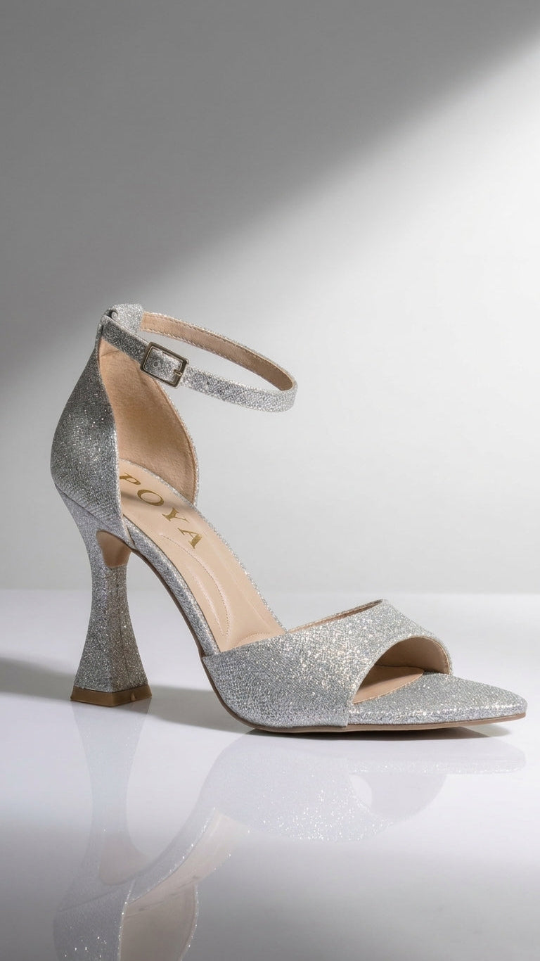 A single silver glitter high-heeled sandal with an ankle strap and open toe, photographed on a clean white reflective surface against a light gray studio background.