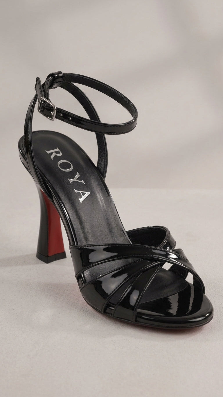 A black patent leather strappy sandal with an ankle strap, a high block heel with a red sole accent, and the brand name ROYA printed on the insole, set against a neutral light gray background.