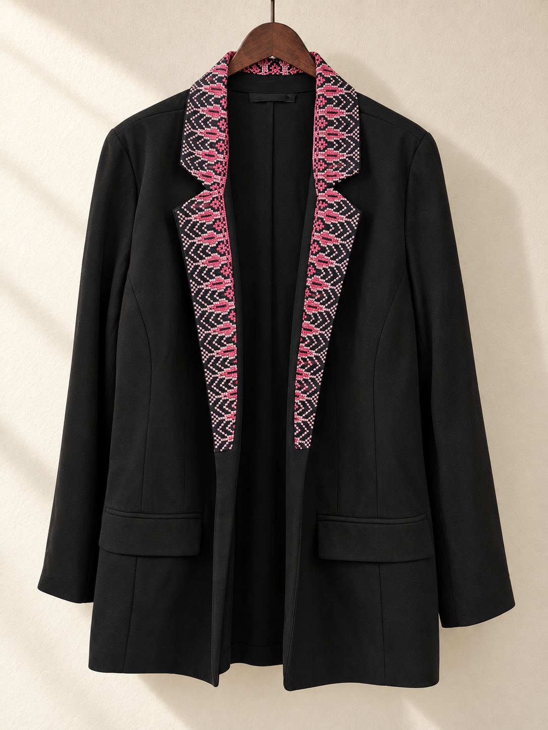 Front view of black blazer with pink embroidered collar and lapels on a wooden hanger