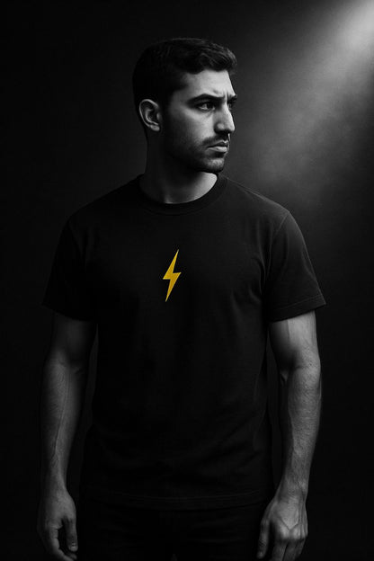 Man wearing a black t-shirt with a yellow lightning bolt design against a dark background