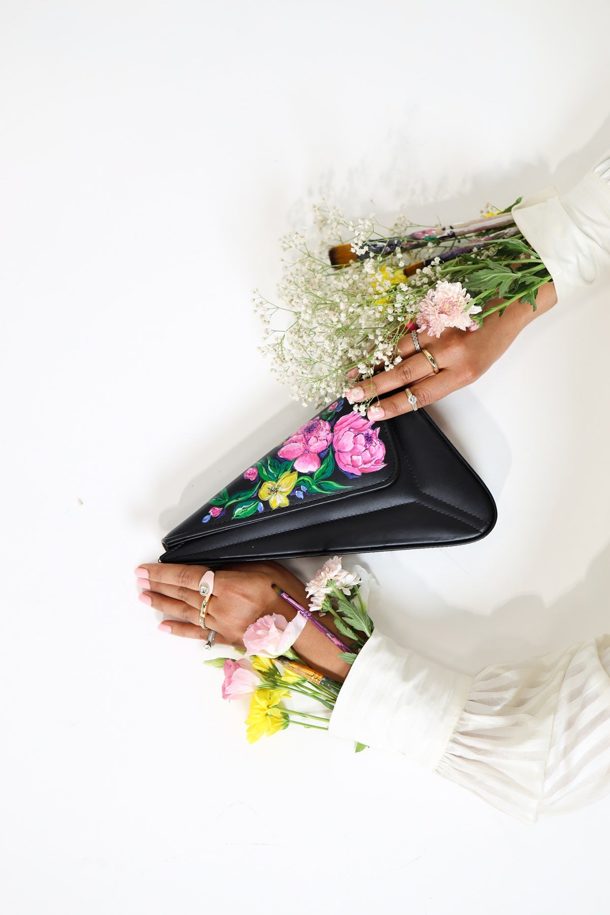 Black clutch with floral design held by a person wearing a white dress.