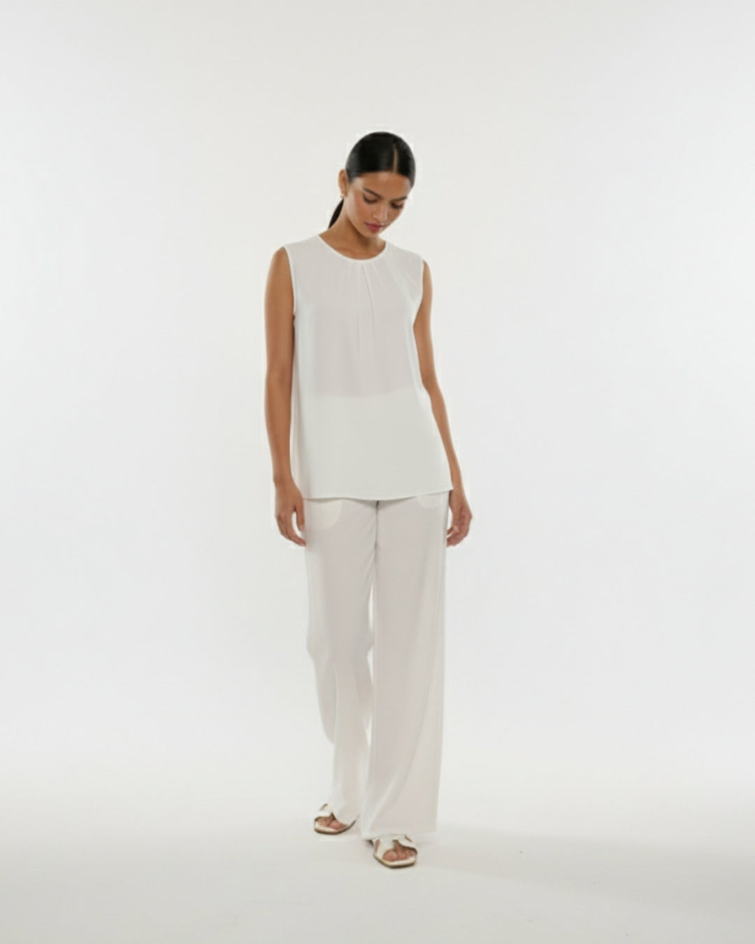 Woman wearing a white sleeveless top and pants on a white background