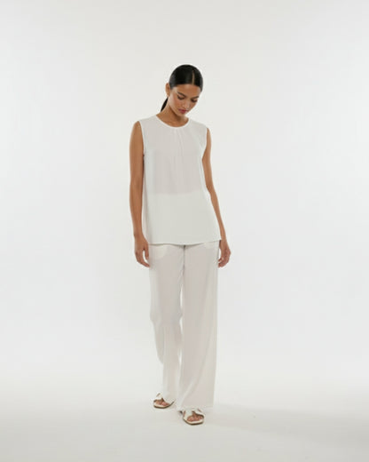 Woman wearing a white sleeveless top and pants on a white background