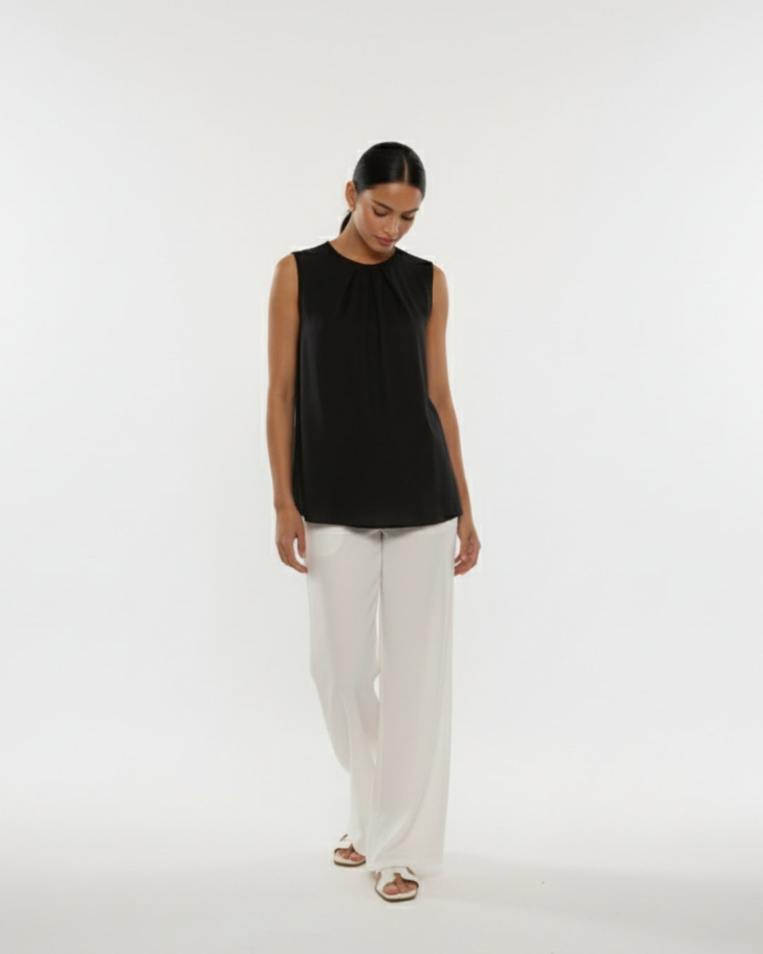 Woman wearing a black sleeveless top and white pants on a white background