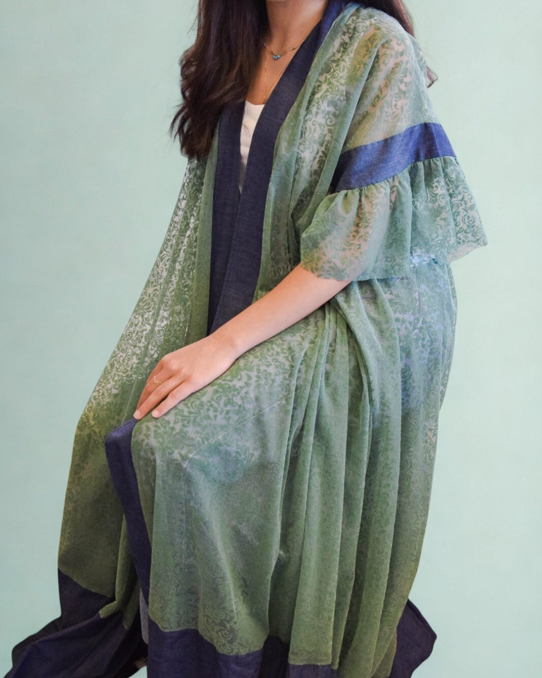 Person wearing a green and navy kimono-style garment against a light green background