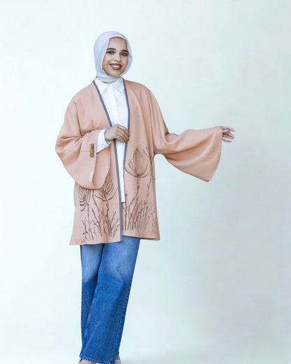 Person wearing a beige cardigan over a white top and blue jeans on a light gray background