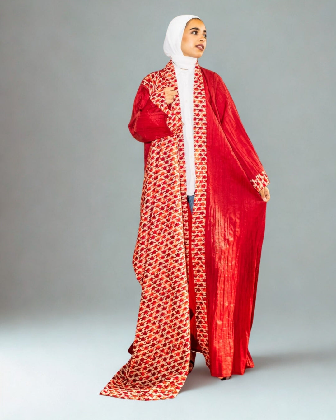 Woman wearing a red and white patterned abaya on a gray background