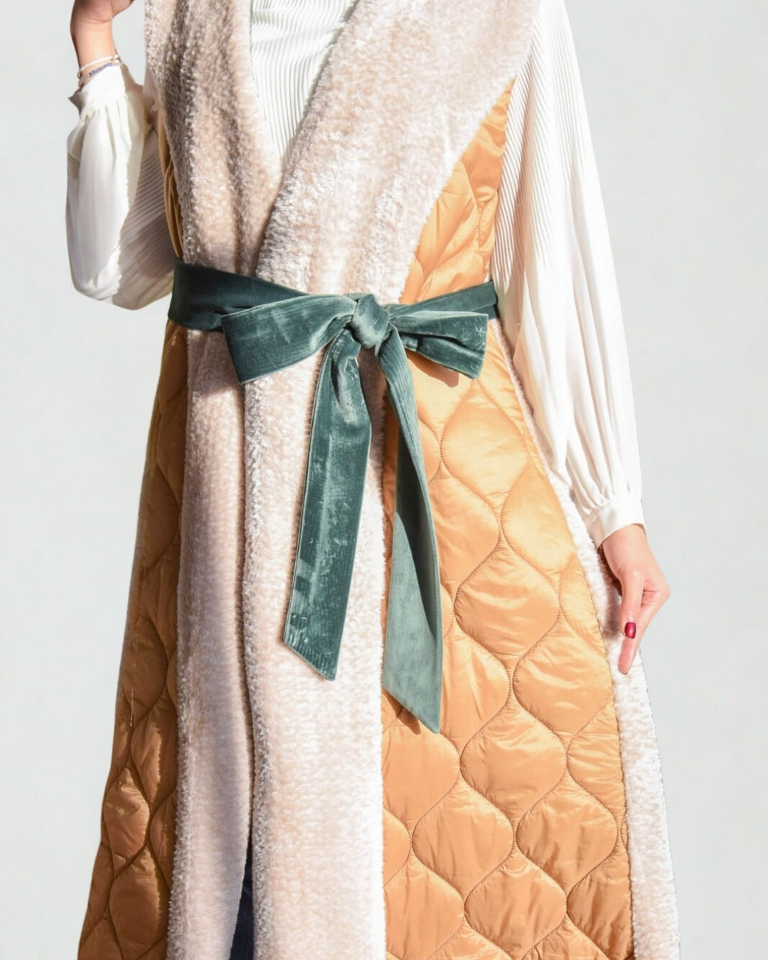 Long quilted coat with a green ribbon on a plain background