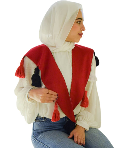 Woman wearing a white hijab, red and black patterned shawl, and blue jeans on a white background