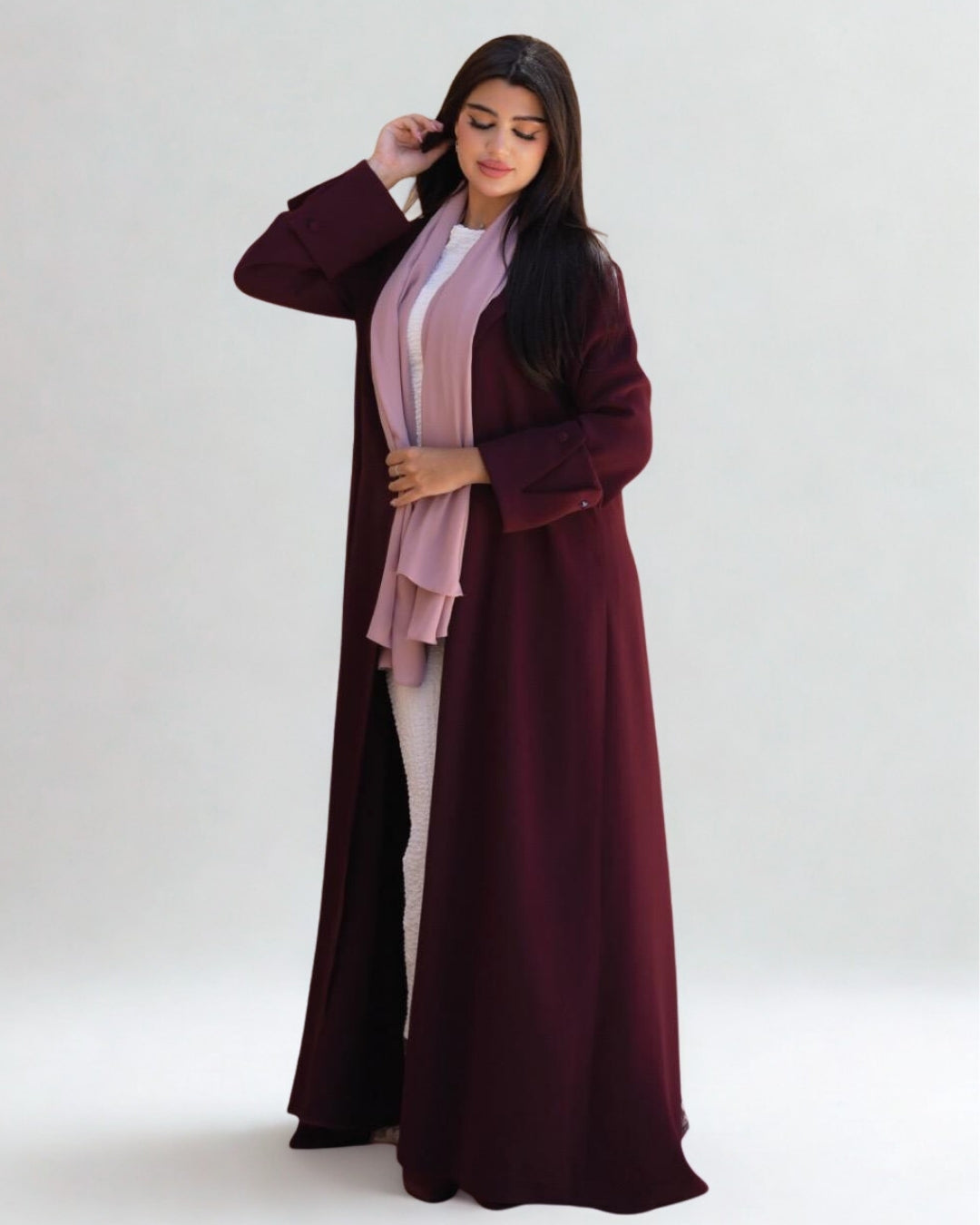 Woman wearing a long burgundy dress with a pink scarf on a white background