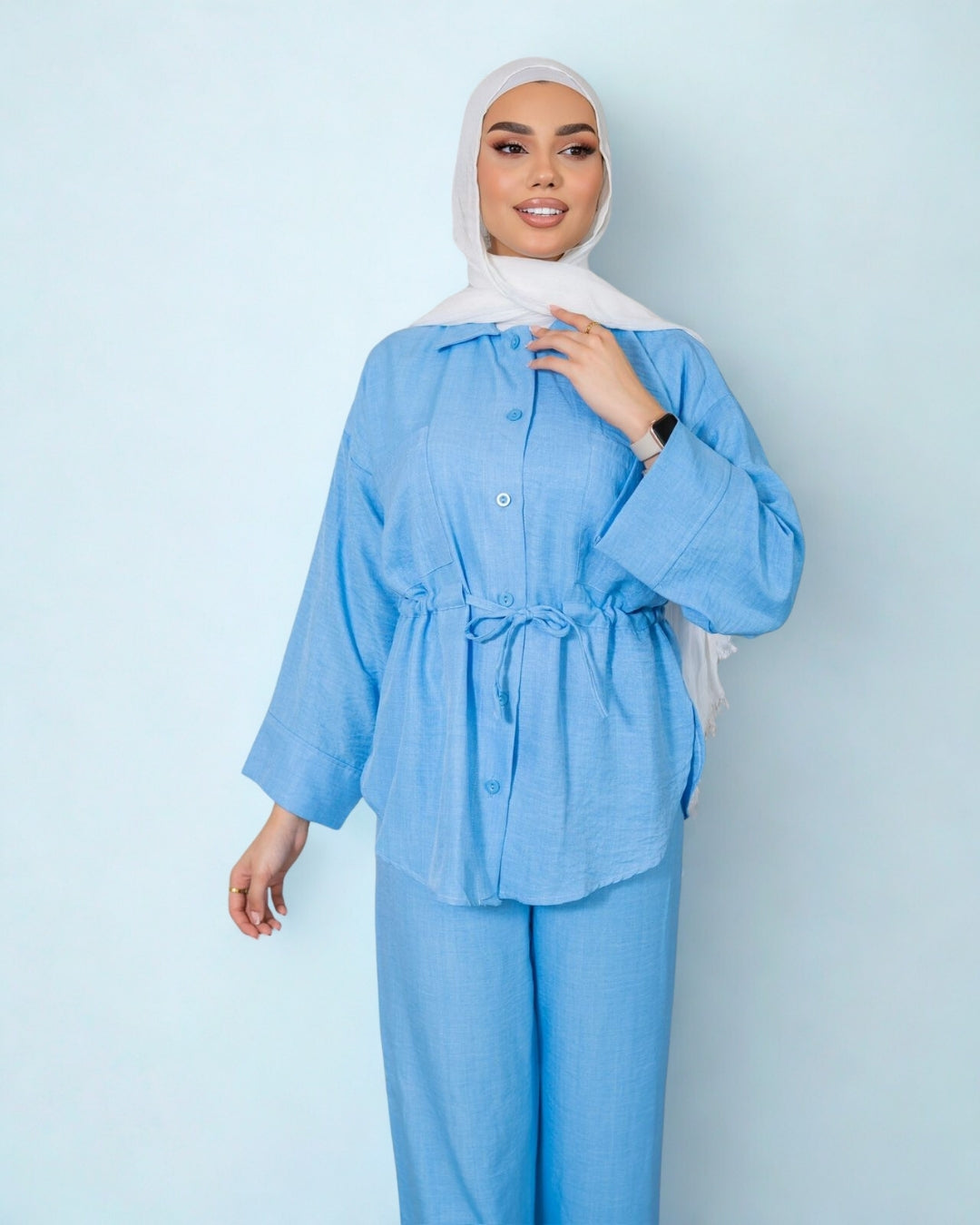 Woman wearing a light blue outfit with a hijab against a light blue background