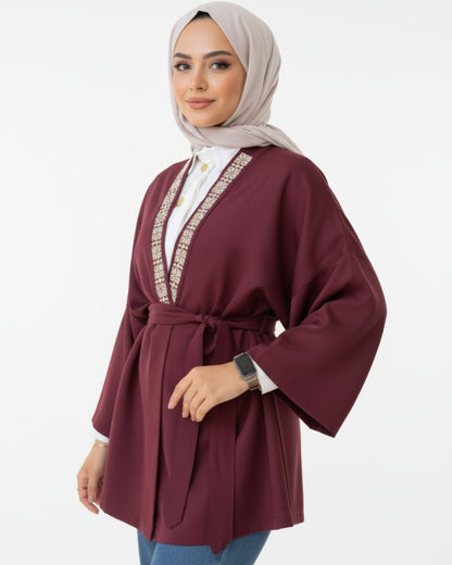 Woman wearing a burgundy abaya with white embroidery on a white background