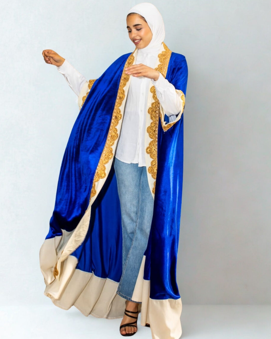 Woman wearing a blue and gold abaya with a white hijab on a light gray background
