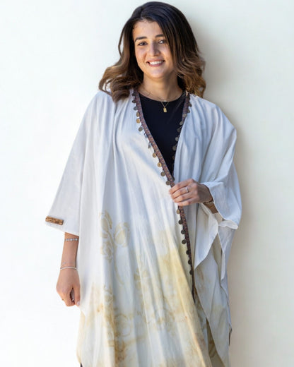 Woman wearing a white and beige patterned shawl against a plain background