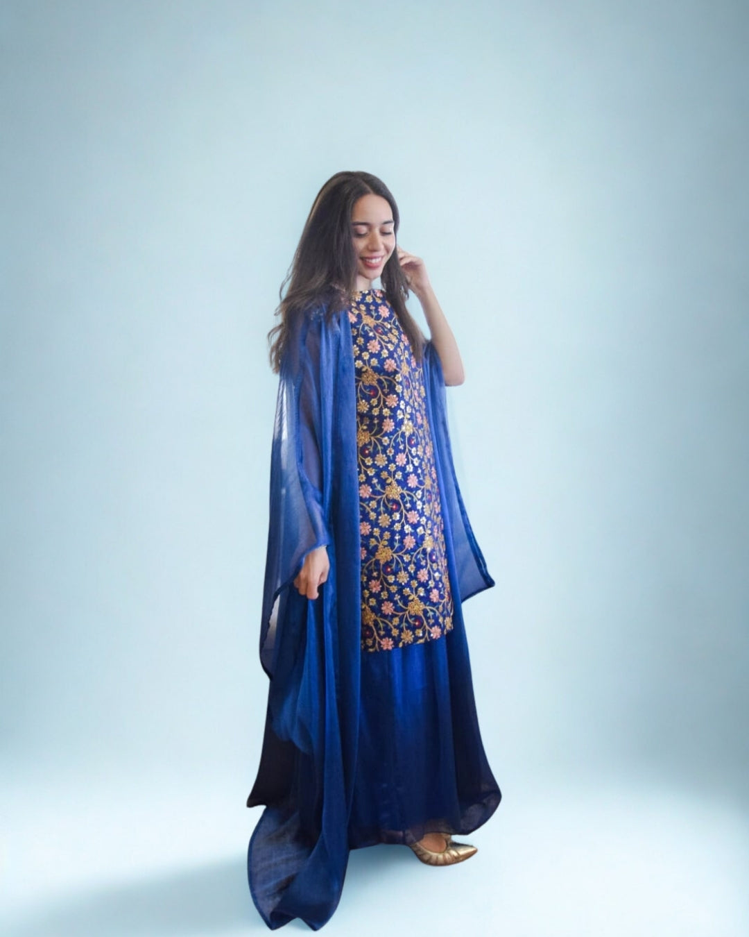 Woman wearing a blue and patterned dress with a matching shawl on a light gray background