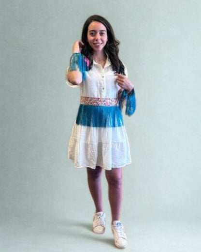 Woman wearing a white dress with blue accents and floral details on a plain background