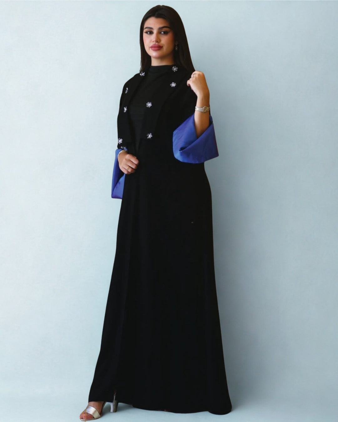 Woman wearing a black dress with blue sleeves against a light gray background