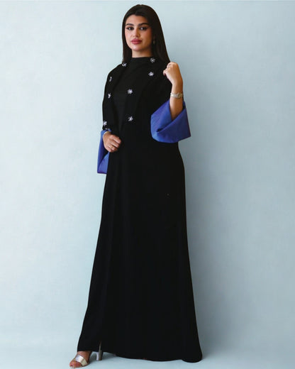 Woman wearing a black dress with blue sleeves against a light gray background