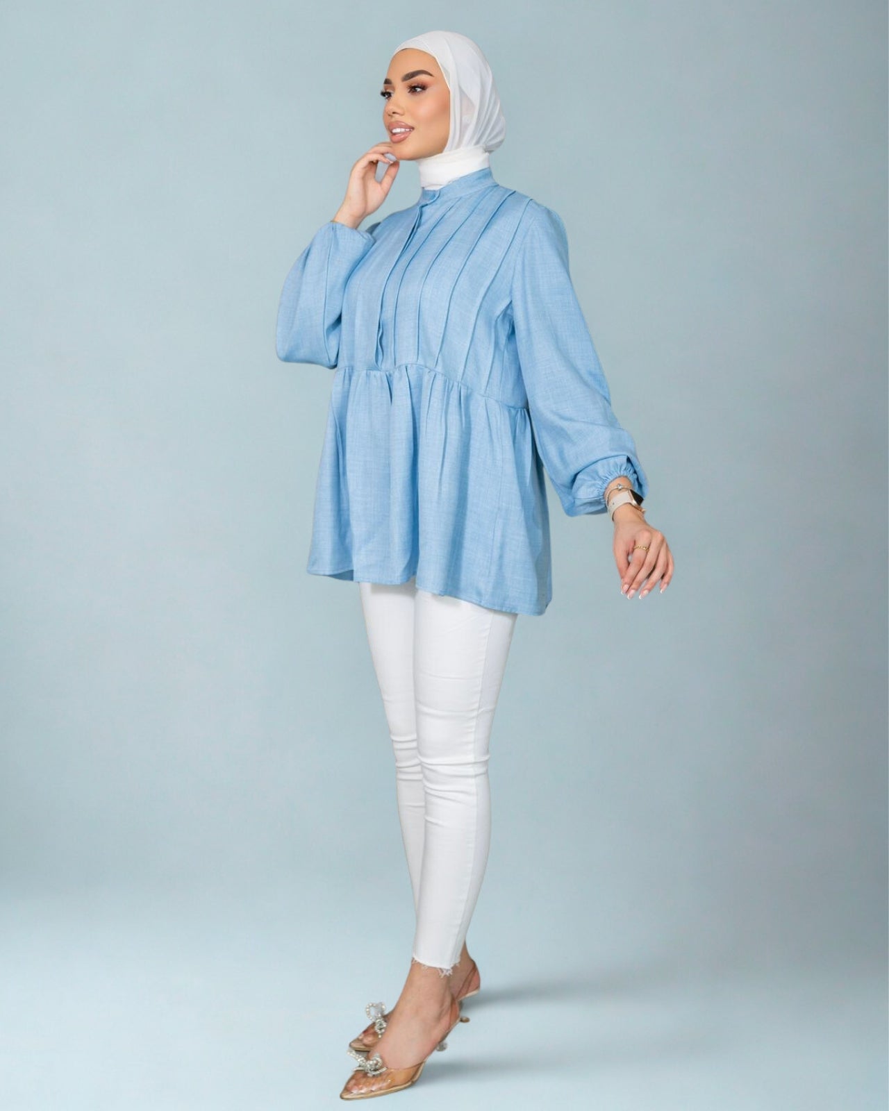 Woman wearing a light blue blouse and white pants on a gray background