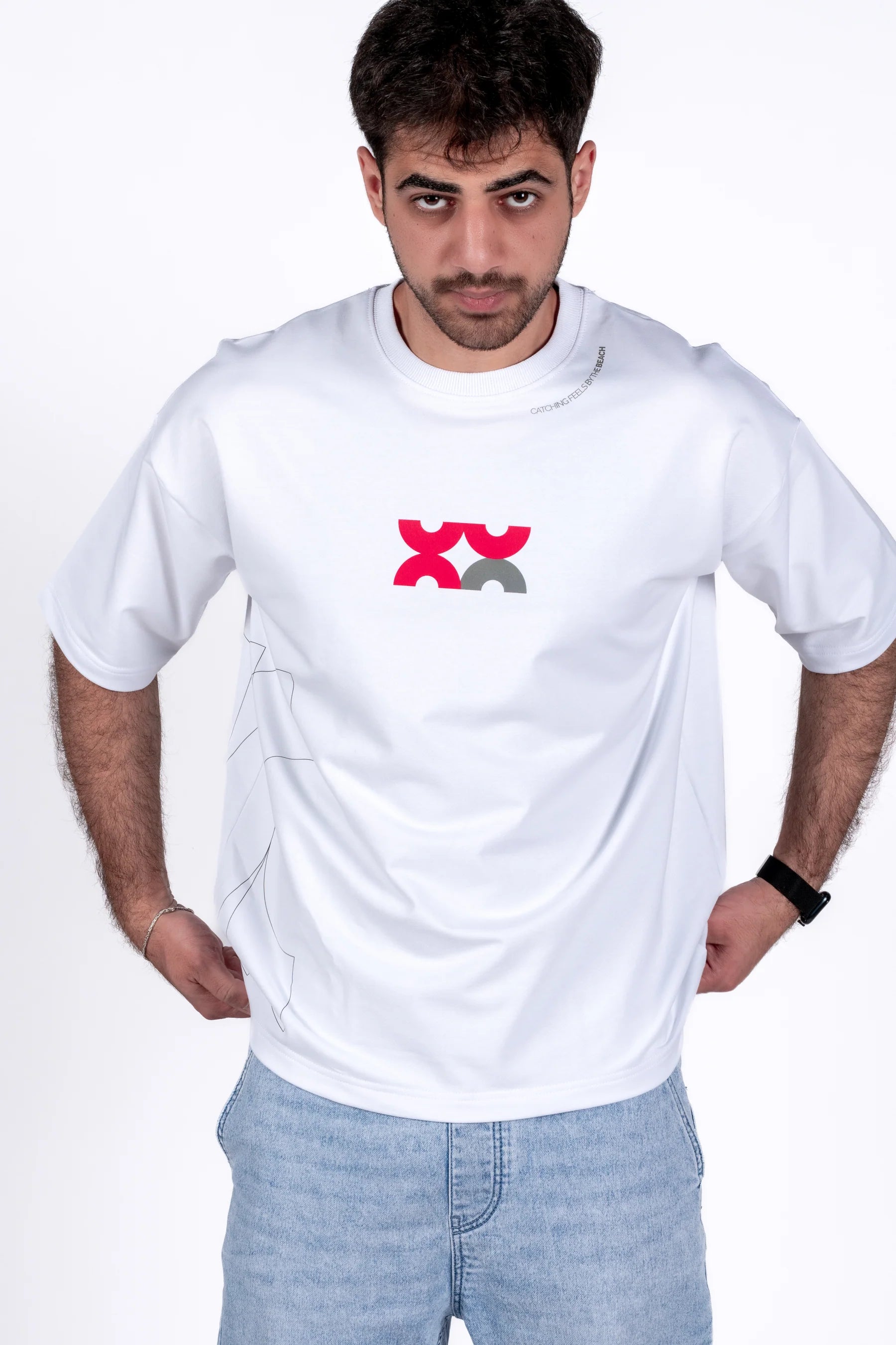 Man wearing a white t-shirt with a red and black logo on a plain background