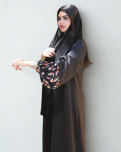 Woman wearing a long dark abaya with floral sleeves against a light background