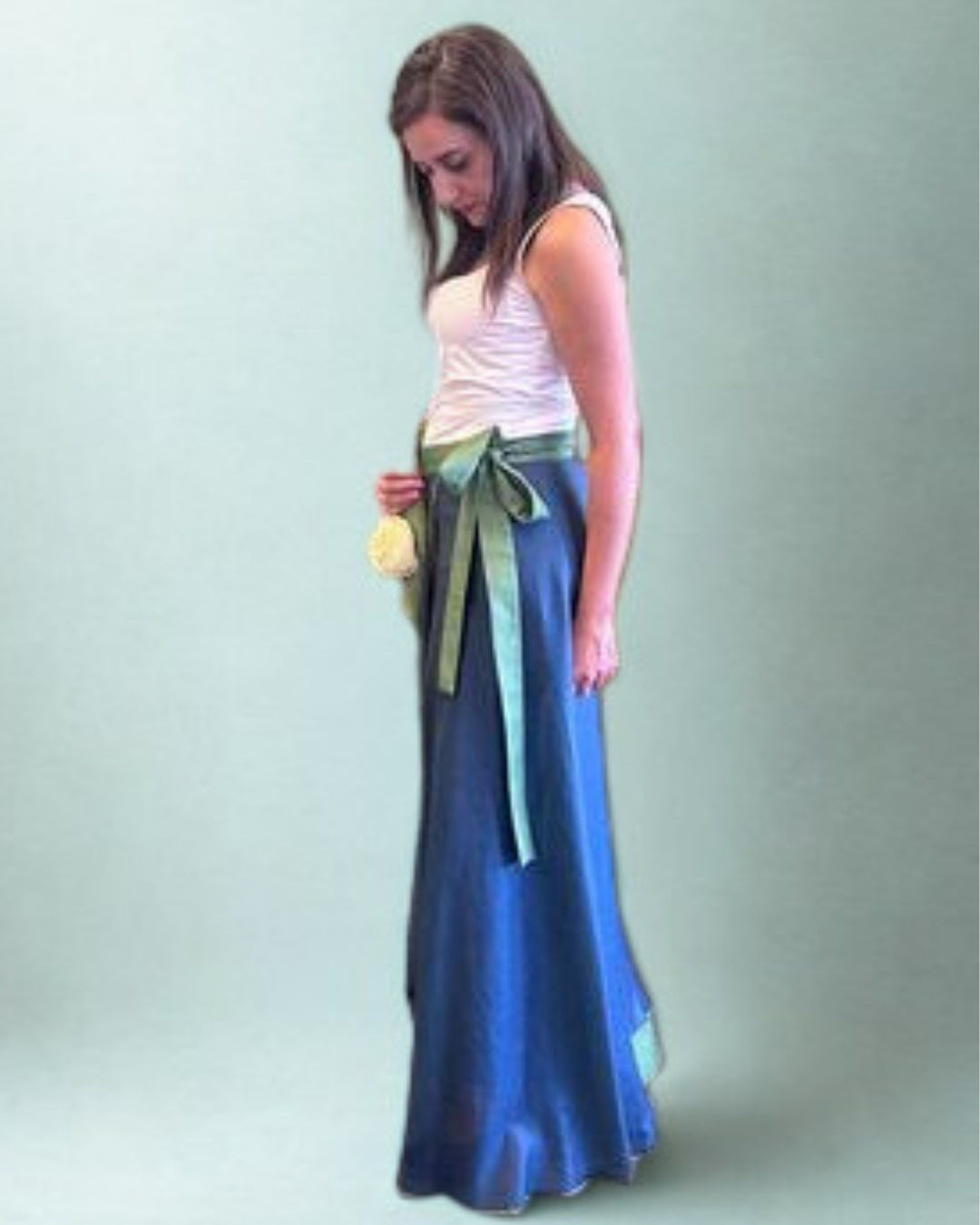Woman wearing a long blue skirt with a green belt against a light gray background