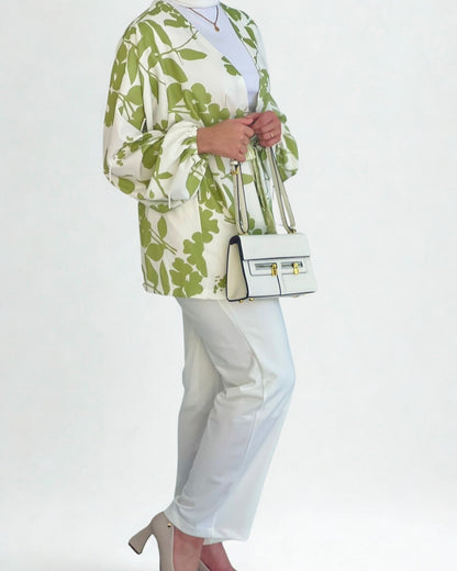 Person wearing a green floral jacket and white pants, holding a white handbag on a light gray background