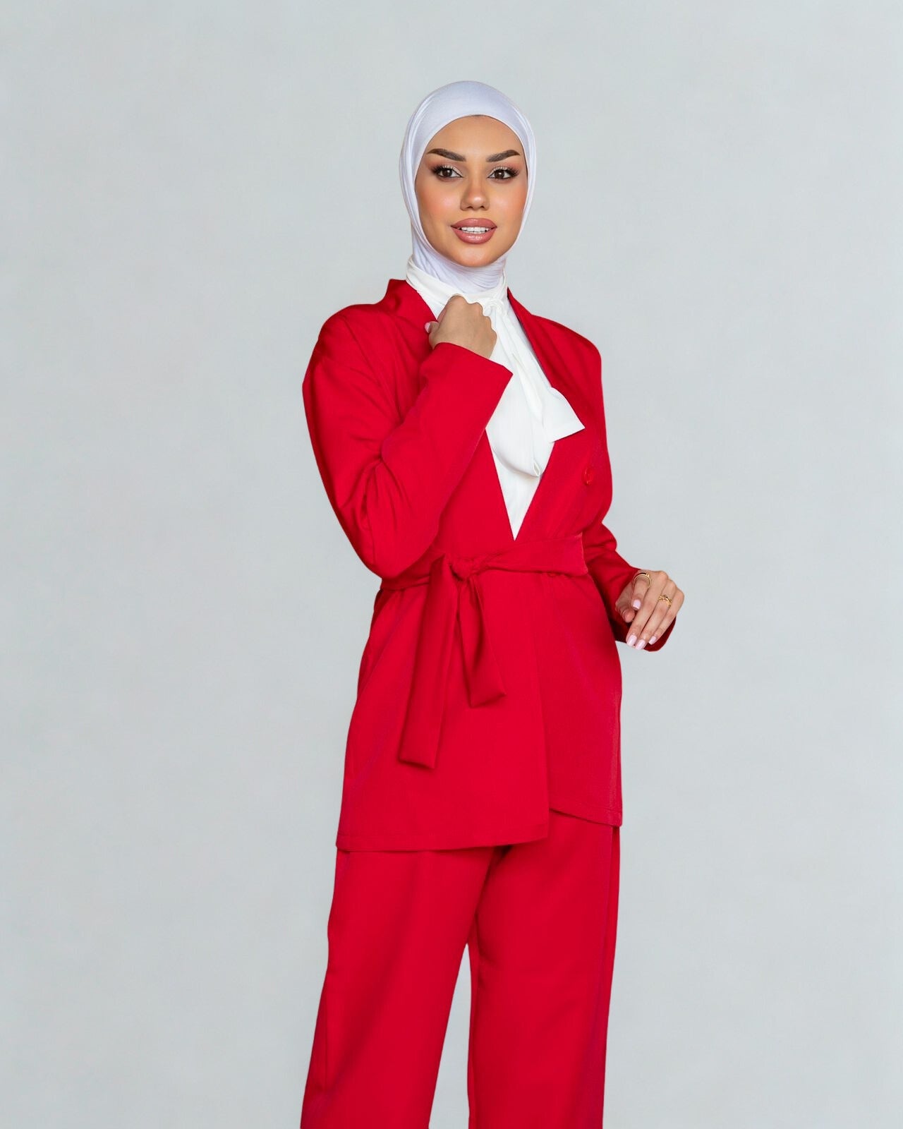 Woman wearing a red outfit with a white hijab on a gray background