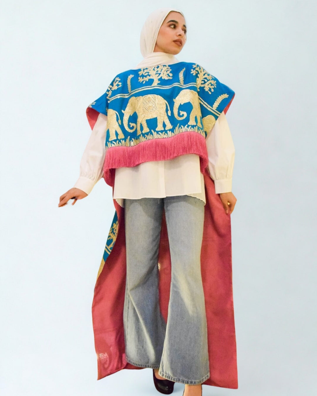 Woman wearing a colorful traditional outfit with elephant patterns on a plain background