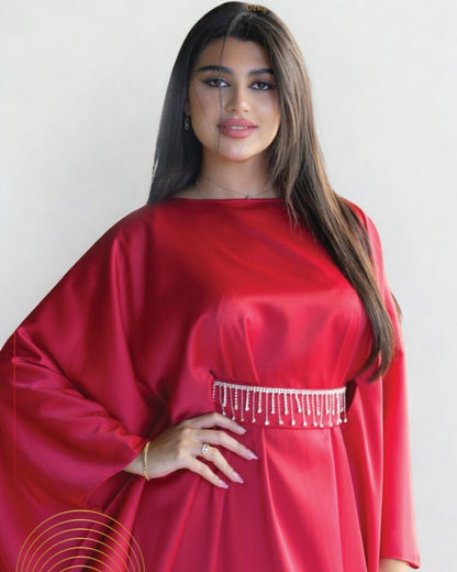 Woman wearing a red dress with a white embellished waistband against a plain background