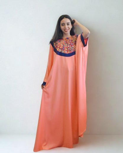 Woman wearing a long, peach-colored dress with an embroidered top against a white background