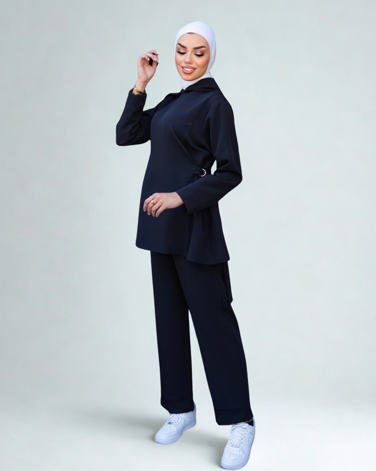 Woman wearing a navy blue outfit with a white hijab on a light gray background