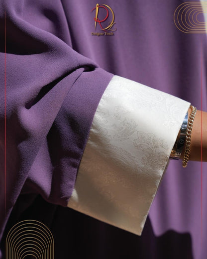 Close-up of a purple garment with a white cuff and gold bracelet on a matching purple background.