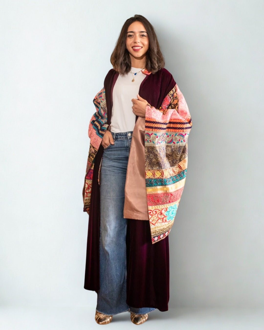 Woman wearing a colorful patterned coat over a white shirt and jeans on a light gray background