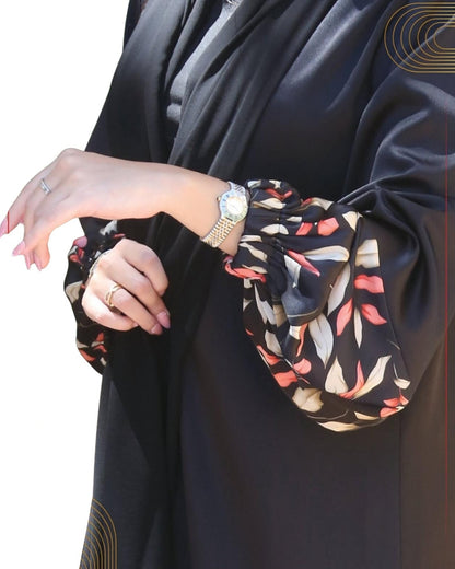 Close-up of a person wearing a black abaya with floral sleeves on a white background