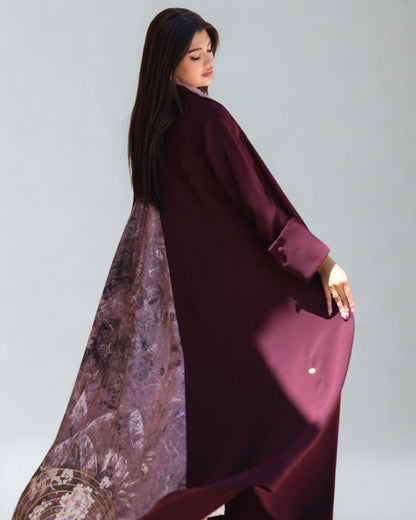 Woman wearing a burgundy abaya with a patterned scarf on a light gray background