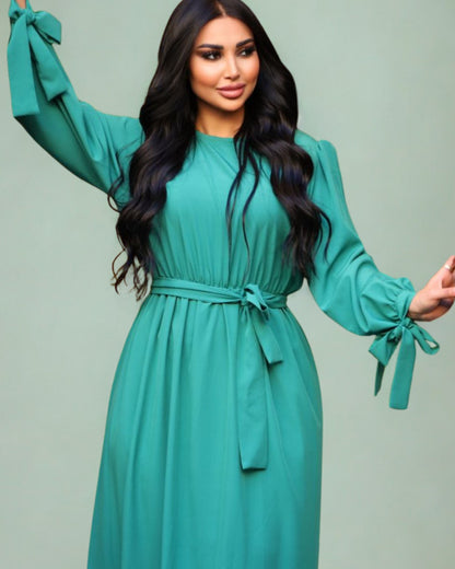 Woman wearing a teal dress with long sleeves against a light green background