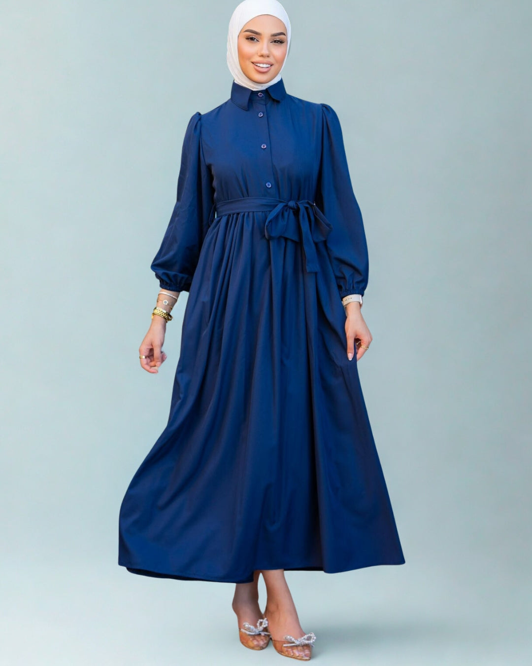 Woman wearing a blue dress with a white hijab on a gray background