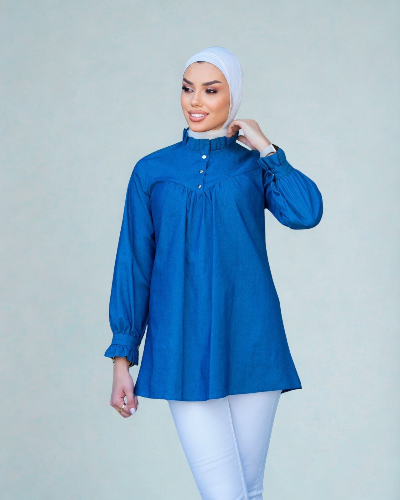Woman wearing a blue blouse and white hijab on a light gray background