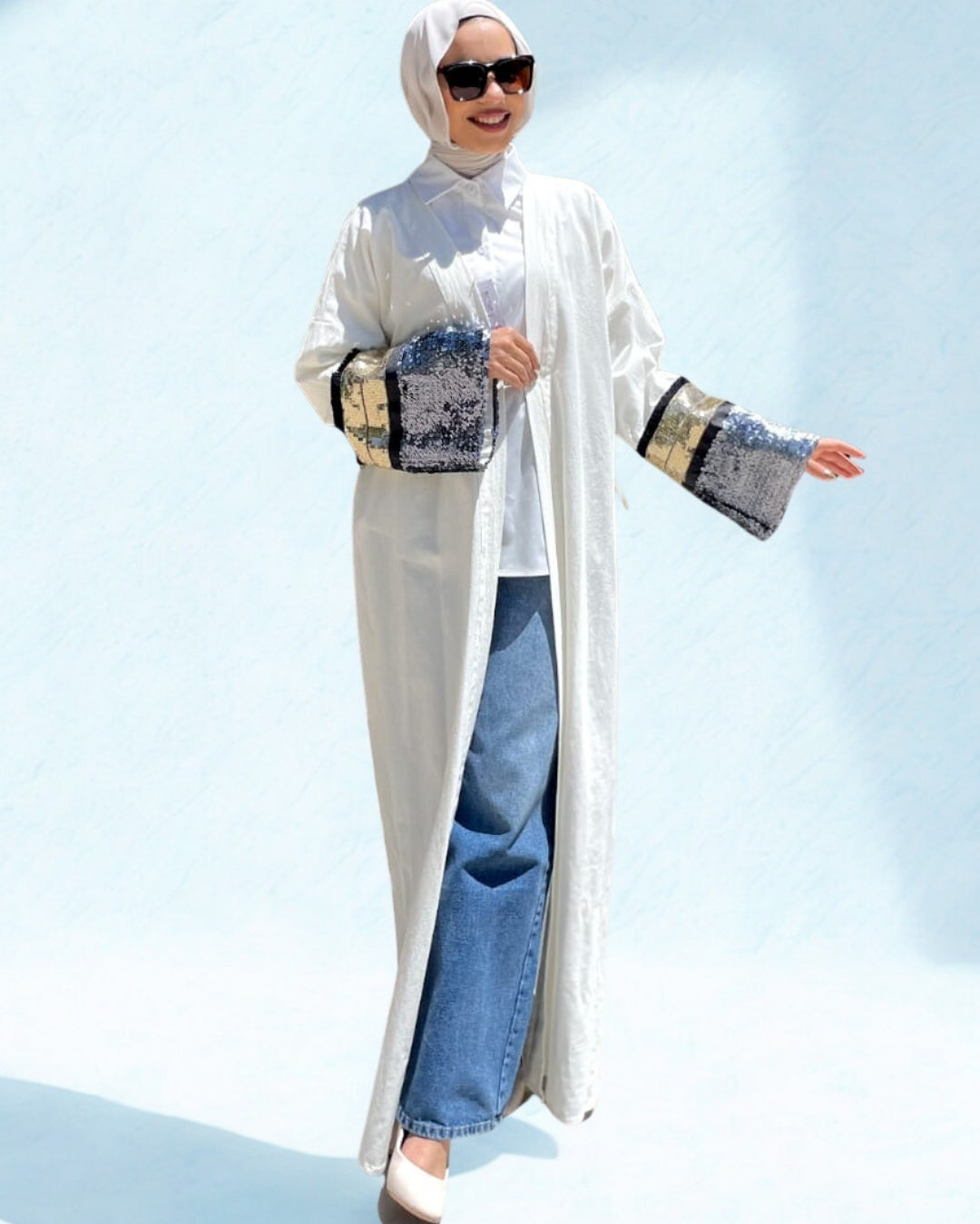 Person wearing a long white garment with patterned sleeves against a clear blue sky.