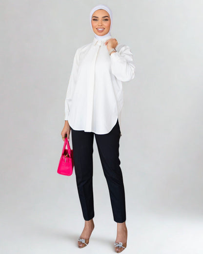 Woman wearing a white blouse, black pants, and a hijab, holding a pink handbag on a white background