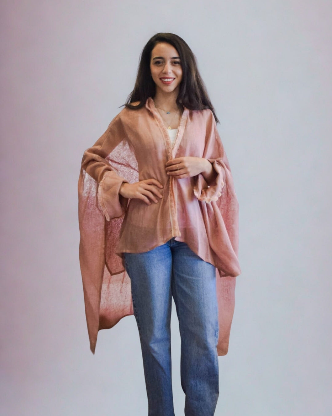 Woman wearing a pink cardigan over a white top and blue jeans against a plain background