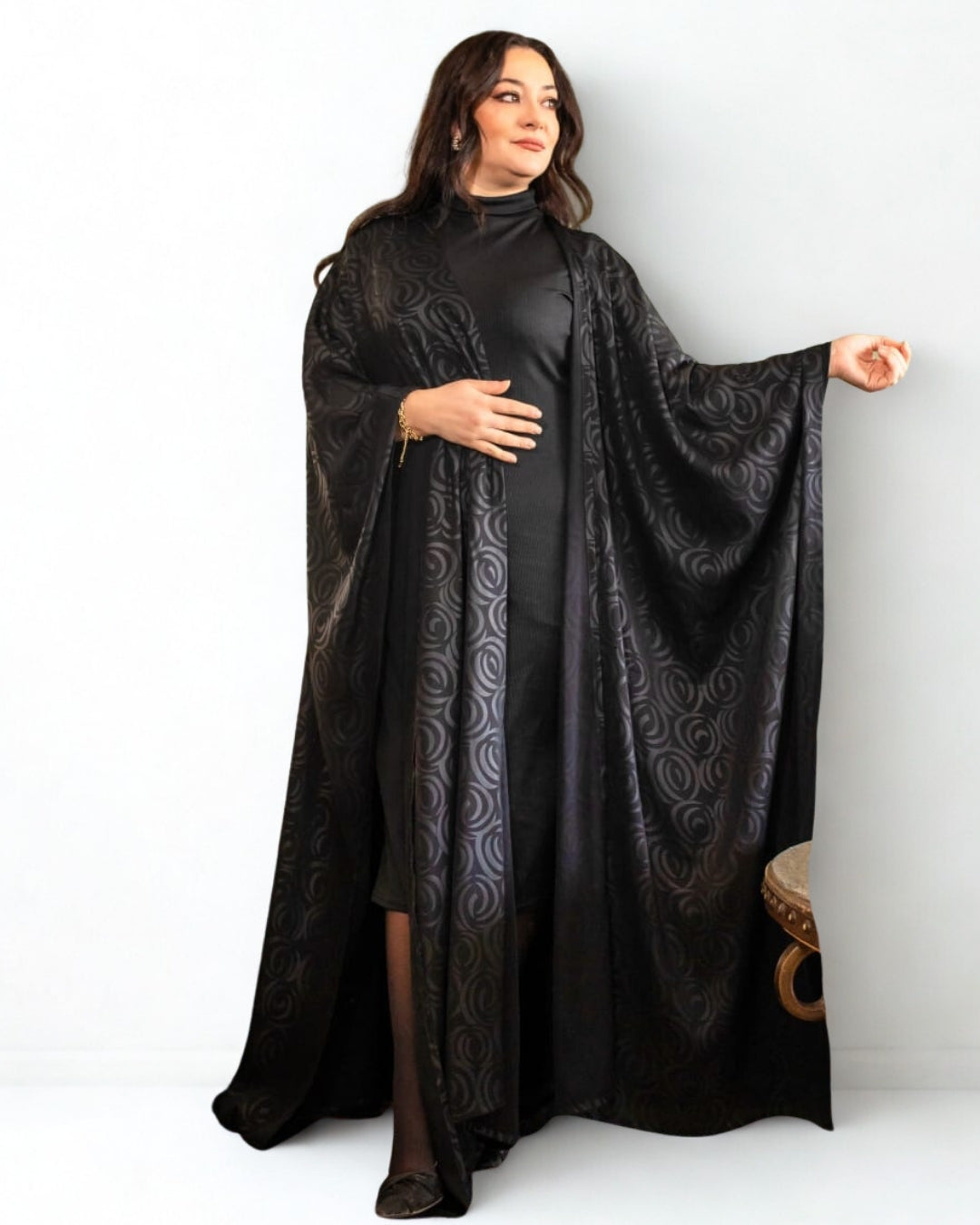 Woman wearing a black dress with a matching cape on a white background