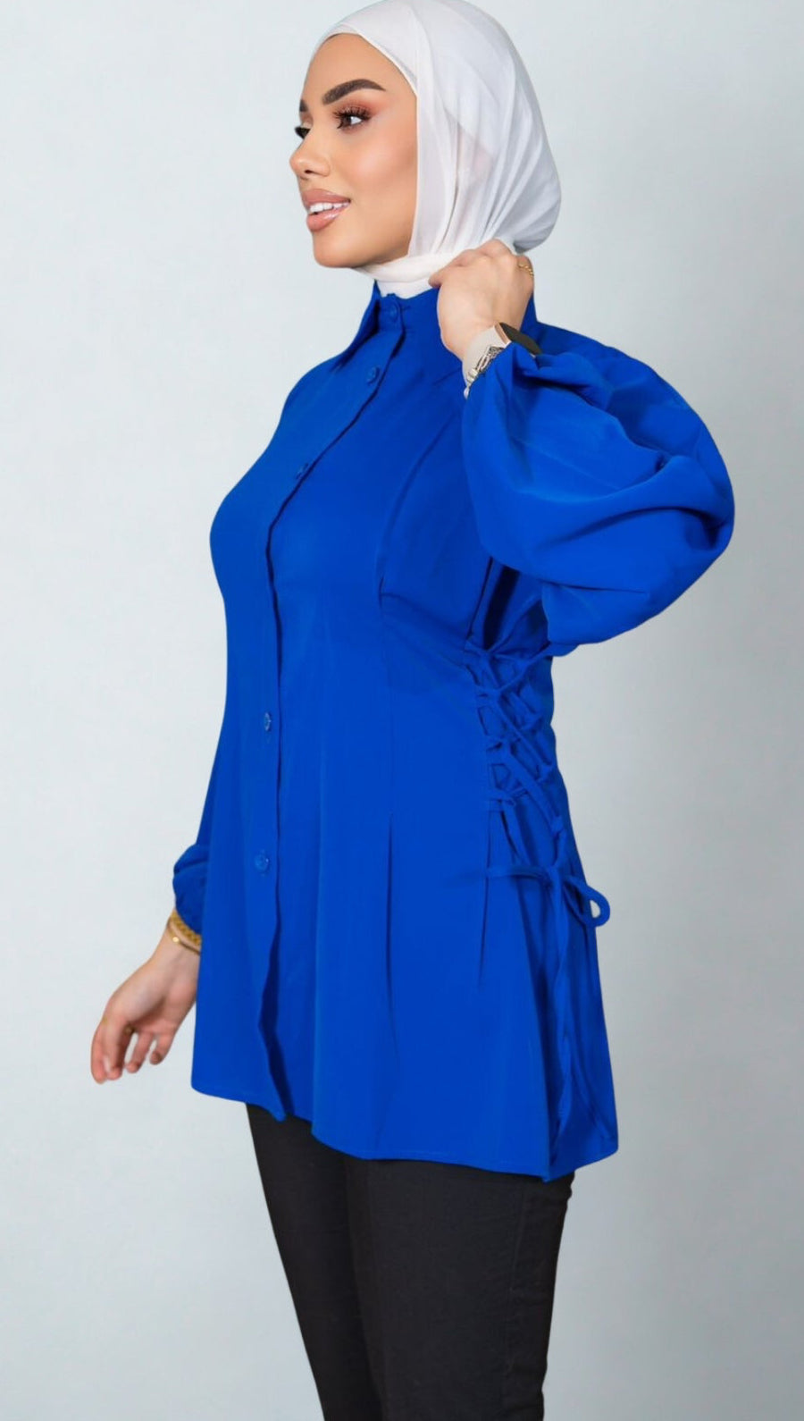 Woman wearing a blue top with a white hijab on a plain background