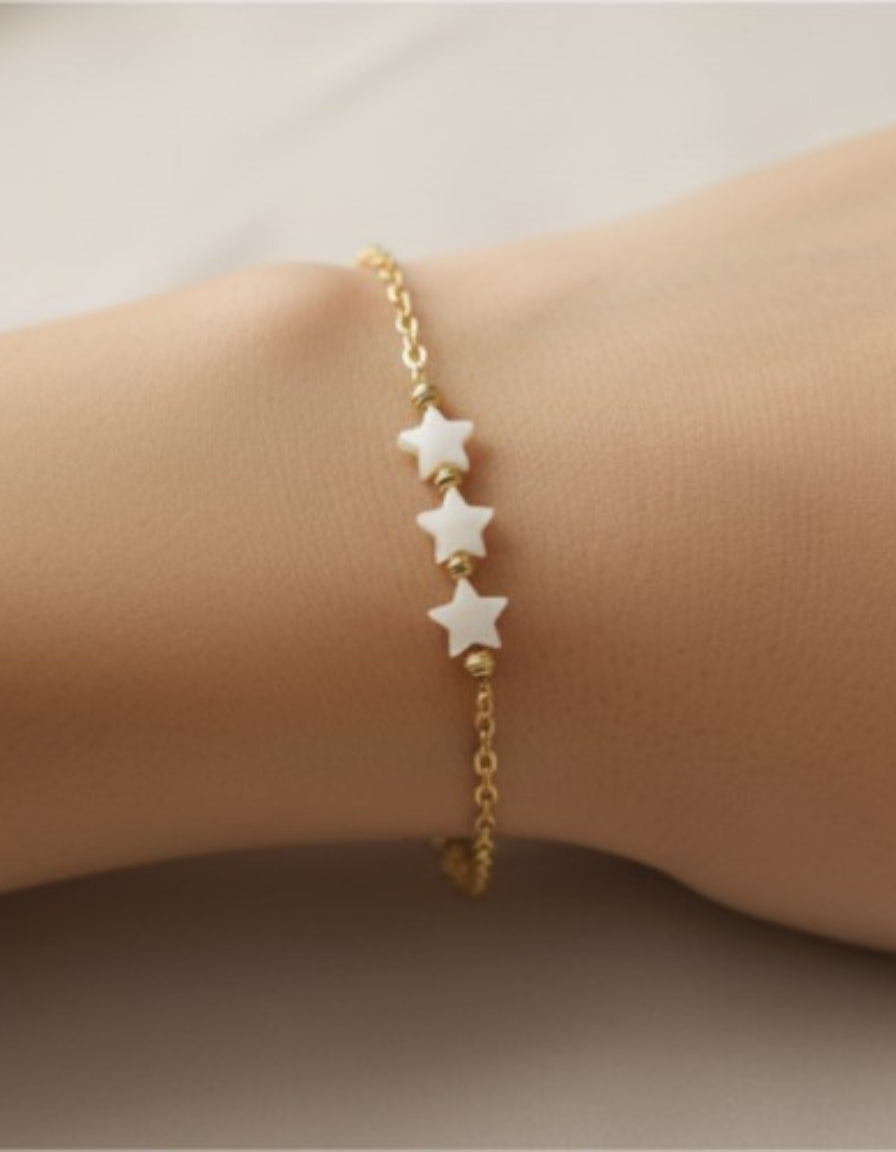 Gold bracelet with star-shaped beads on a wrist against a neutral background
