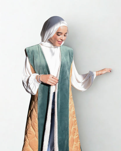 Woman wearing a green and beige abaya with a white hijab on a light gray background