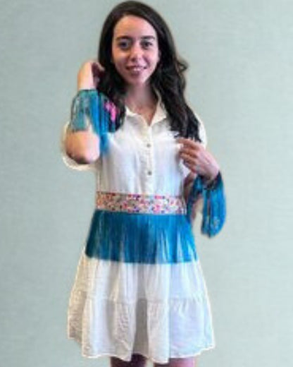 Woman wearing a white dress with blue accents and floral details on a plain background