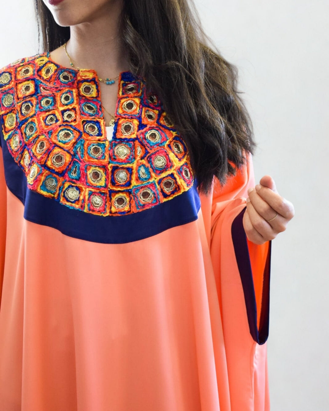 Woman wearing a colorful embroidered top with a plain background